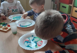 Zosia, Miłosz i Szymek zanurzają patyczki kosmetyczne z płynem do mycia naczyń w mleku tworząc wir.