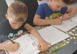Kacper i Oskar wykonują zadania w kartach pracy.