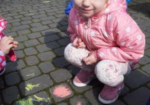 Kornelia maluje kredą na chodniku.