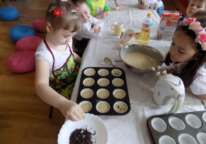 Zosia posypuje swoją babeczkę wiórkami czekoladowymi.