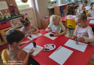 Piotr, Lena, Hania i Zosia K. malują pnie drzew.