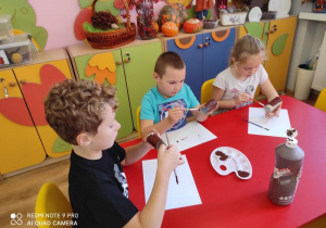 Eryk, Arthur i Gabi malują pnie drzew.