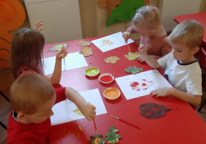 Lilka, Filip, Tymon i Nikola tworzą jesienne kompozycje przy pomocy liści.