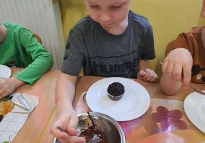 Jacek pokrywa czekoladą swoją muffinkę.