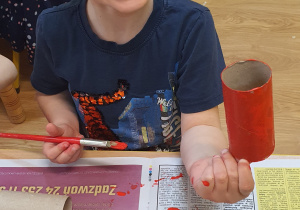 Piotruś maluje rolkę papierową na kolor czerwony.
