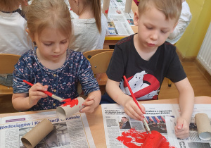 Nelka i Jacuś malują rolkę papierową na kolor czerwony.