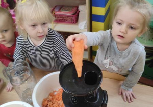 Oliwia wkłada marchewkę do wyciskarki.