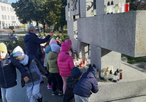 Dzieci z grupy Pszczółki zapalają znicze pod pomnikiem Poległych Harcerek i Harcerzy.