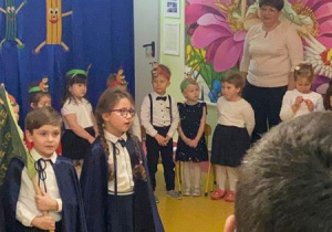 Dzieci stoją z proporcem przedszkolnym i śpiewają hymn Calineczki.