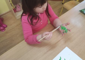 Marysia maluje dłoń zielona farbą.
