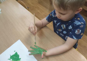 Tadzio maluje dłoń zielona farbą.