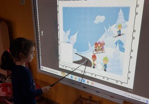 Matylda przy tablicy interaktywnej wskazuje niebezpieczne zabawy zimowe dzieci.