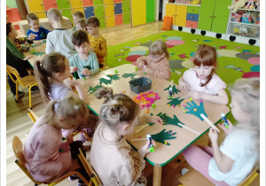 grupa dzieci wykleja kolorową bibułą szablon rączek