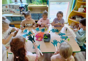 grupa dzieci wykleja kolorową bibułą szablon rączek