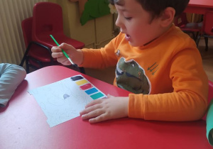 Maksymilian maluje farbami obrazek dinozaura