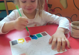 Lenka maluje farbami obrazek dinozaura