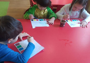 Dzieci malują farbami obrazki dinozaura