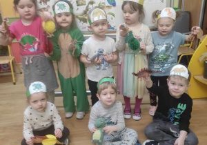 Dzieci ustawione przed dekoracją prezentują swoje stroje i przyniesione dinozaury.
