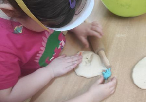 Dzieci bawią się masą solną: wyciskają figurki dinozaurów.