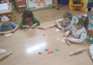 Dzieci bawią się masą solną: Wałkują i wyciskają figurki dinozaurów.