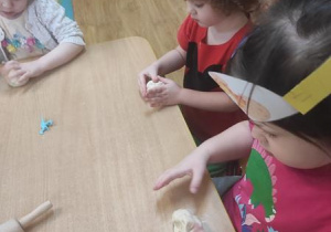 Dzieci bawią się masą solną: formują owal i chowają w nim figurki dinozaurów.