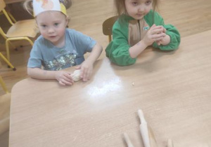 Dzieci bawią się masą solną: formują owal i chowają w nim figurki dinozaurów.