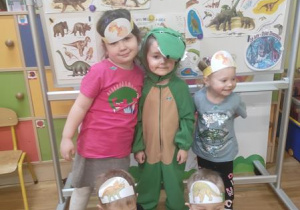 Dzieci pozują z dinusiem Adą w kolorowych opaskach na głowach.