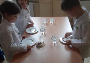 Zosia, Lilka i Szymon układają kolorowe cukierki na talerzach.