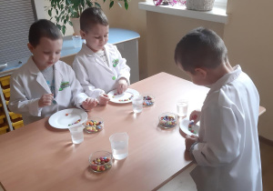 Kuba, Witek i Adam układają kolorowe cukierki na talerzach.