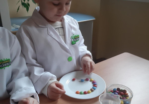 Witek układa kolorowe cukierki na swoim talerzu.
