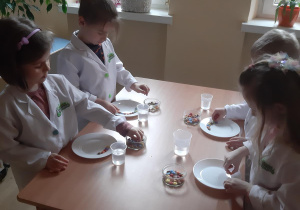 Zosia, Mateusz, Antek i Kornelka układają kolorowe cukierki na talerzach.