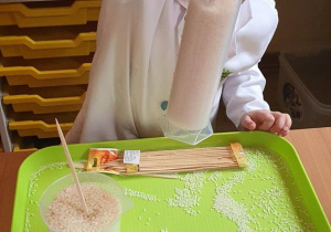 Witek podnosi zlewkę z ubitym ryżem trzymając jedynie za patyczek umieszczony w środku.