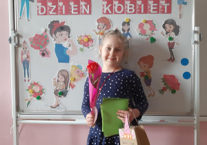 Zuzia prezentuje swoje upominki- laurkę, medal, prezent oraz tulipana.