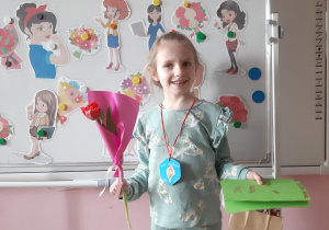 Kornelia prezentuje swoje upominki- laurkę, medal, prezent oraz tulipana.