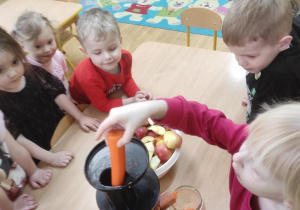 Dzieci wykonują sok marchewkowo- jabłkowy. Zosia K. wkłada do wyciskarki marchewkę