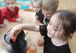 Dzieci wykonują sok marchewkowo- jabłkowy. Ada wkłada do wyciskarki jabłko.