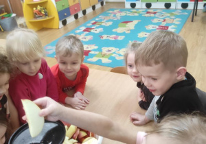 Dzieci wykonują sok marchewkowo- jabłkowy. Nikola wkłada do wyciskarki jabłko.