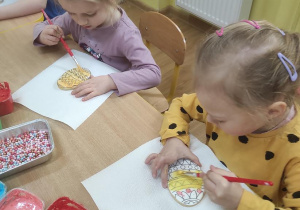Dzieci malują kolorowym lukrem ciasteczka w kształcie pisanek.