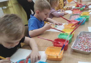 Dzieci malują kolorowym lukrem ciasteczka w kształcie pisanek.