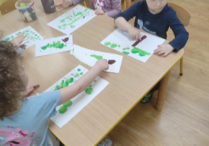 Dzieci malują drzewo.