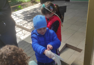 Dzieci zakładają jednorazowe rękawiczki i wychodzą sprzątać teren wokół przedszkola.