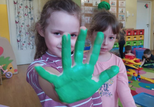 Hania odciska rękę pomalowaną zieloną farbą, która później zostanie wykorzystana jako liść