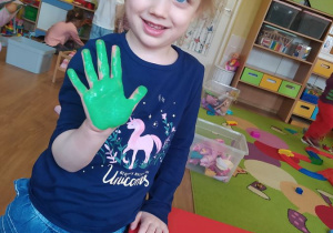 Emilka odciska rękę pomalowaną zieloną farbą, która później zostanie wykorzystana jako liść
