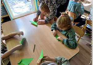 Dzieci składają zielony papier techniką origami, tak by powstał liść