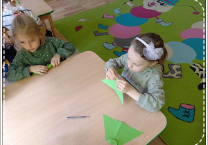 Nela i Idalia składają zielony papier techniką origami, tak by powstał liść