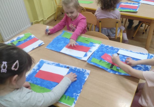 Dzieci wykonują pracę plastyczną - flagę Polski na tle łąki