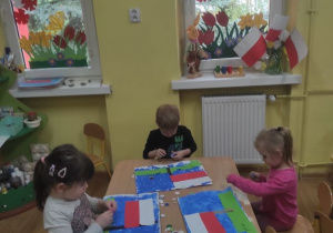 Dzieci wykonują pracę plastyczną - flagę Polski na tle łąki