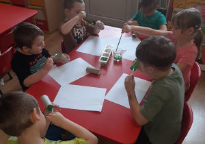 Adam, Witek, Kuba, Mateusz, Lilka i Kuba malują tubki po papierze na zielono aby zrobić z nich liście.