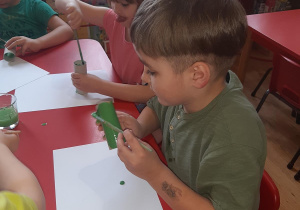 Kuba, Lilka i Mateusz malują tubki po papierze na zielono aby zrobić z nich liście.