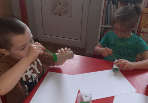 Kuba i Mateusz malują tubki po papierze na zielono aby zrobić z nich liście.